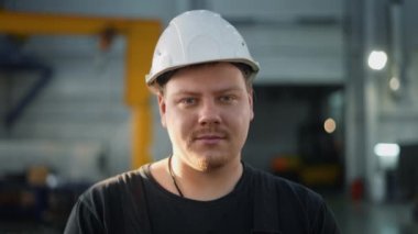 Kasklı tamirci dikkatle kameraya bakıyor. Birkaç saniye sonra gülümsemeye başlıyor..