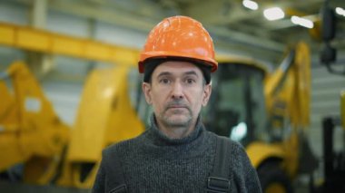 Parçalanmış bir kazıcının arka planına bakan kasklı bir tamirci kameraya dikkatlice bakar. Sonra gülümsedi..