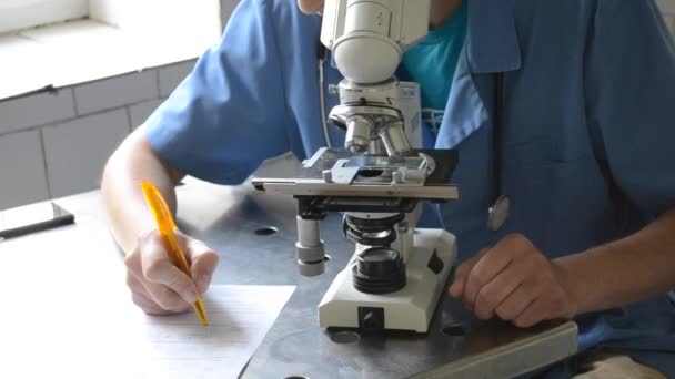 Доктор пишет на форме и микроскопе — стоковое видео