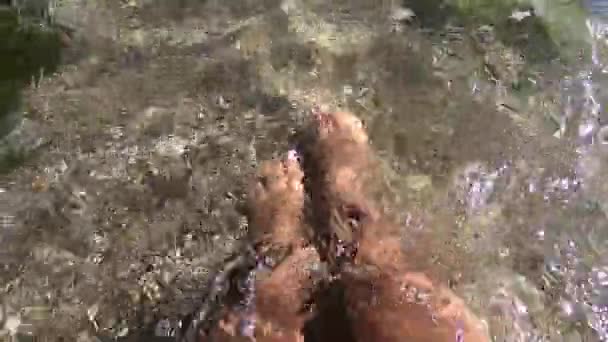 Twee vrouwelijke voeten zijn in schoon en transparant water op zandstrand — Stockvideo