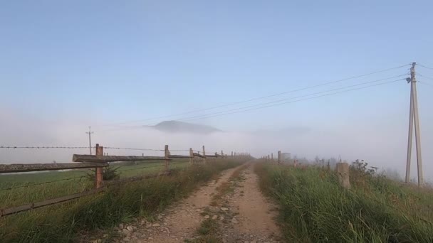 Man wandelt langs onverharde pad op bergtop, waaronder er 's morgens mist — Stockvideo