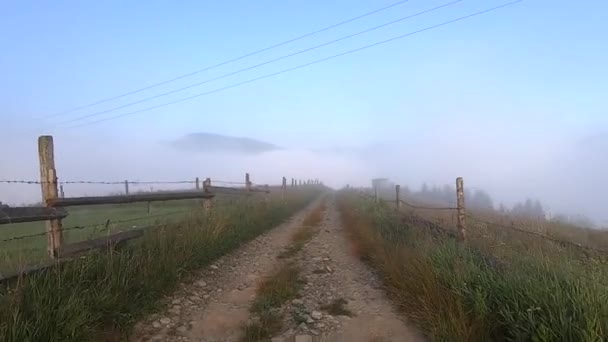 El hombre camina por el camino de tierra en la cima de la montaña, bajo el cual hay niebla matutina — Vídeo de stock