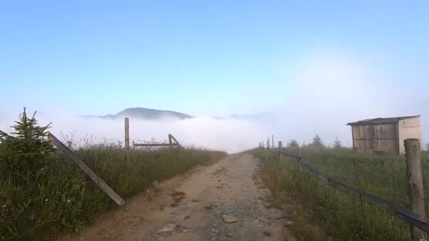 El hombre camina por el camino de tierra en la cima de la montaña, bajo el cual hay niebla matutina — Vídeo de stock