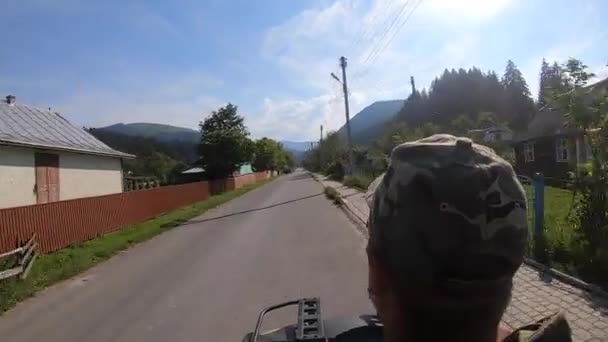 Man rijdt zwarte quad fiets of ATV op de weg in het bergdorp in de zomer — Stockvideo