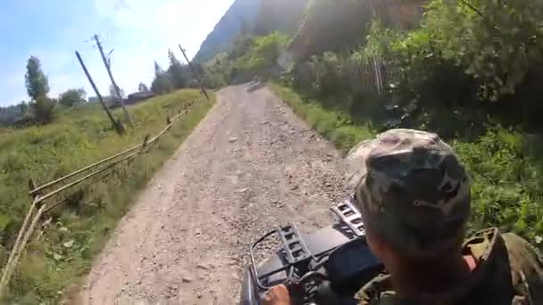 男は山の村の未舗装道路上の黒いクワッドバイクやATVに乗る — ストック動画