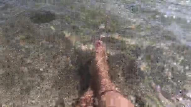 Deux pieds féminins sont dans l'eau propre et transparente sur la plage de sable fin — Video