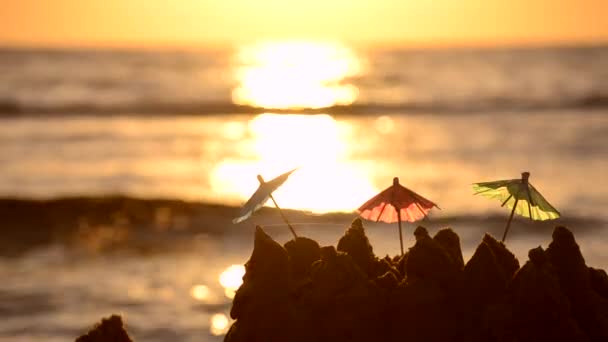 Kleine Sonnenschirme aus Papier stehen bei Sonnenaufgang im Sand am Sandstrand — Stockvideo