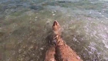 İki kadın ayakları deniz kıyısındaki kumlu sahilde şeffaf sularda.