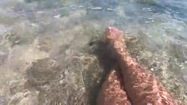 Twee vrouwelijke voeten zijn in schoon transparant water op zandstrand aan de kust — Stockvideo