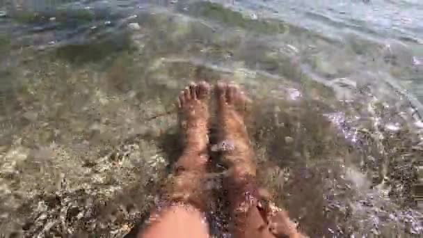 2人の女性の足は海岸の砂浜の透明な水の中にあります — ストック動画
