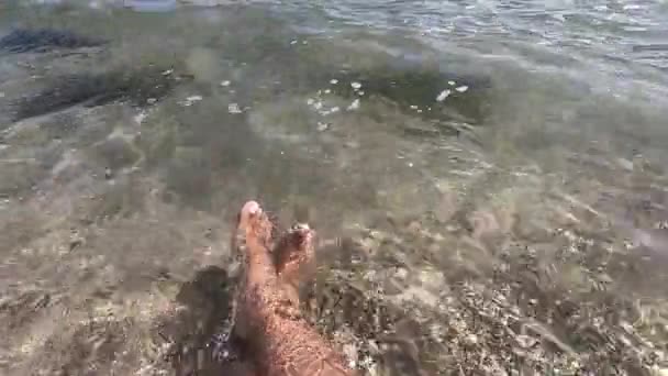 Dos pies femeninos están en agua limpia y transparente en la playa de arena en la orilla del mar — Vídeos de Stock