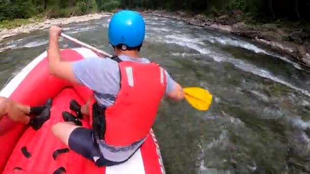 Rafting. Erkekler kırmızı şişme kayıkta oturur, kürek çeker ve dağ nehrinde yüzer. — Stok video