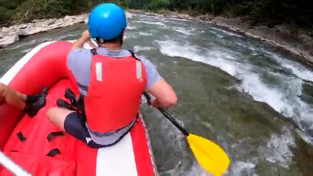 Rafting. Muži sedí v červené nafukovací lodi, pádlo a plovoucí horské řece — Stock video