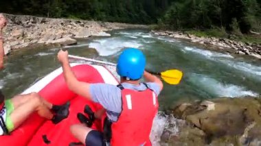 Rafting. Erkekler kırmızı şişme kayıkta oturur, kürek çeker ve dağ nehrinde yüzer.