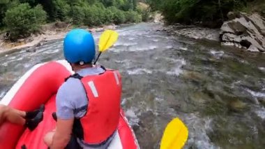 Rafting. Erkekler kırmızı şişme kayıkta oturur, kürek çeker ve dağ nehrinde yüzer.