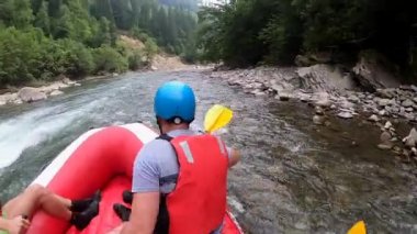 Rafting. Erkekler kırmızı şişme kayıkta oturur, kürek çeker ve dağ nehrinde yüzer.