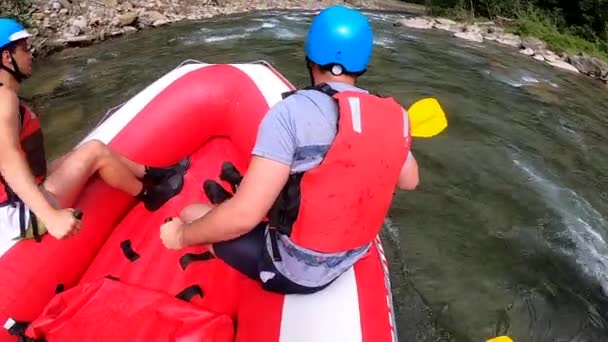 Rafting. Erkekler kırmızı şişme kayıkta oturur, kürek çeker ve dağ nehrinde yüzer. — Stok video