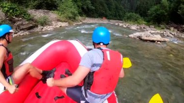 Rafting. Erkekler kırmızı şişme kayıkta oturur, kürek çeker ve dağ nehrinde yüzer.