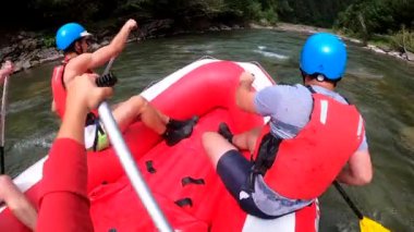 Rafting. Erkekler kırmızı şişme kayıkta oturur, kürek çeker ve dağ nehrinde yüzer.