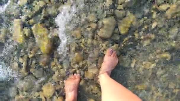 Chica camina con los pies desnudos sobre piedras en un río rocoso poco profundo en las montañas — Vídeo de stock