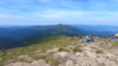 Arka plan bulanık. İnsanlar dağın tepesinde oturur ve manzaraya hayran kalırlar.