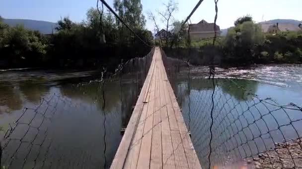 Człowiek chodzący most wiszący nad rzeką — Wideo stockowe