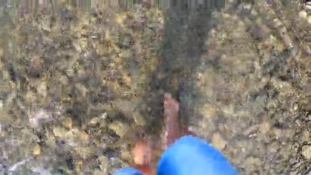 Девушка ходит босиком по камням мелкой реки крупным планом, солнечный летний день — стоковое видео