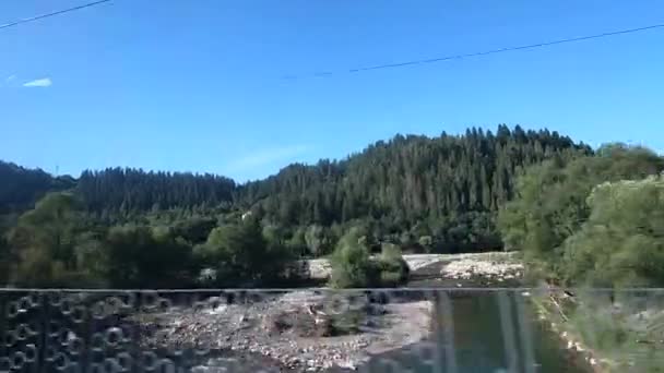 Vista da janela do autocarro. Carro está dirigindo na estrada em montanhas da floresta e da cidade — Vídeo de Stock