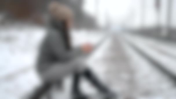 Unscharfer Hintergrund. Ein Mädchen sitzt auf Schienen mit einer Tasse Tee-Thermoskanne — Stockvideo