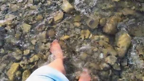 Chica camina con los pies desnudos sobre piedras en un río rocoso poco profundo en las montañas — Vídeo de stock