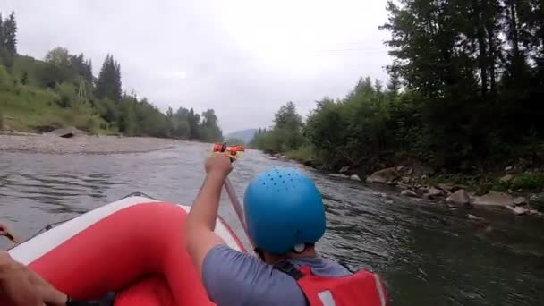Люди сідають у надувний каучуковий човен і пливуть вниз гірською річкою. — стокове відео