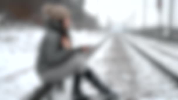 模糊的背景。一个女孩坐在铁轨上，手里拿着一大杯热茶 — 图库视频影像