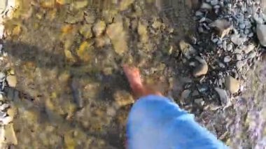 Sığ nehir taşlarının üzerinde çıplak ayakla yürüyen bir kız. Yakın, güneşli bir yaz günü.