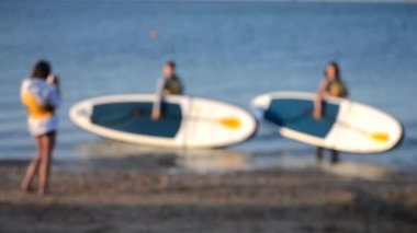Arka plan bulanık. Birçok insan denizde durup yemek masasıyla fotoğraf çekiyor.