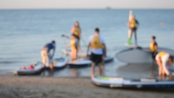 Oklar bakgrund. Många människor står och sitter och simmar på sup boards — Stockvideo