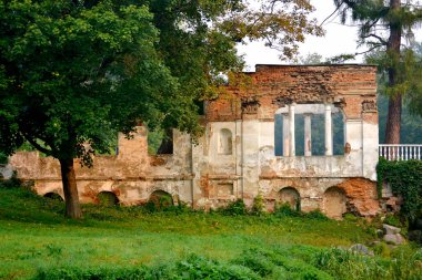 Parkta sütunlu beyaz parmaklıklı kırmızı tuğlalar ve ağaç kalıntıları.
