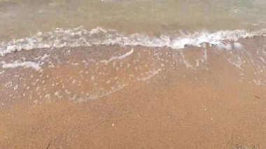 Beyaz köpüklü şeffaf su dalgaları kumların üzerinde akıyor.