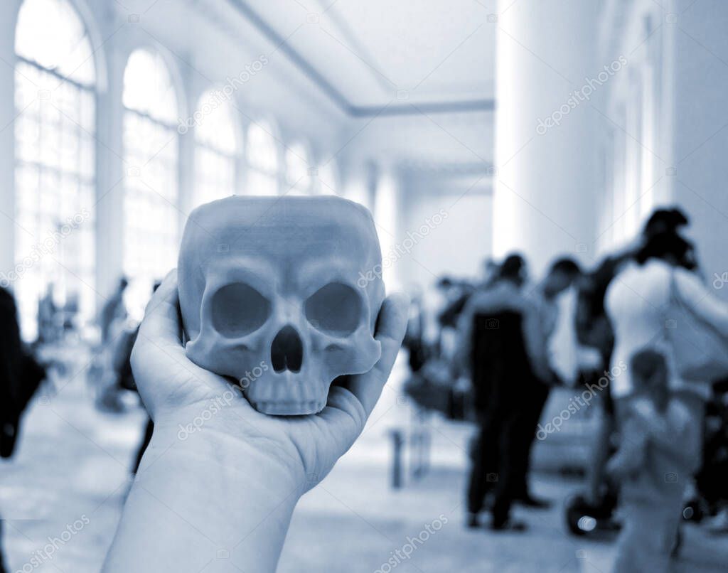 Skull printed on 3d printer in mans hand. On the back of a blurry plan - people