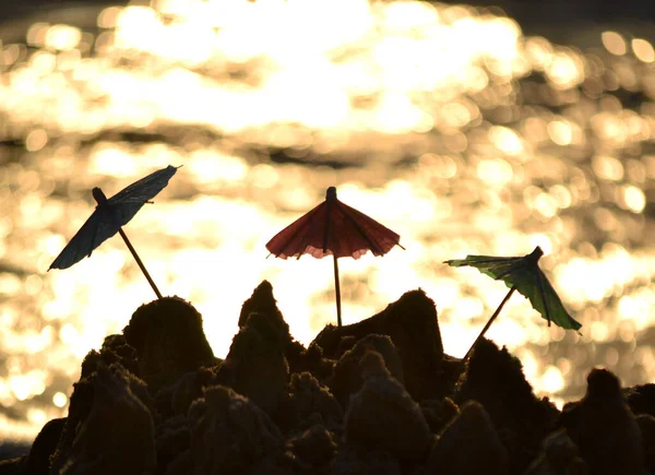 Três pequenos guarda-sóis de praia feitos de papel para coquetel na areia — Fotografia de Stock