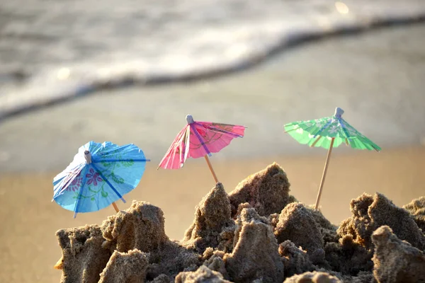 Três pequenos guarda-sóis de praia feitos de papel para coquetel na areia — Fotografia de Stock