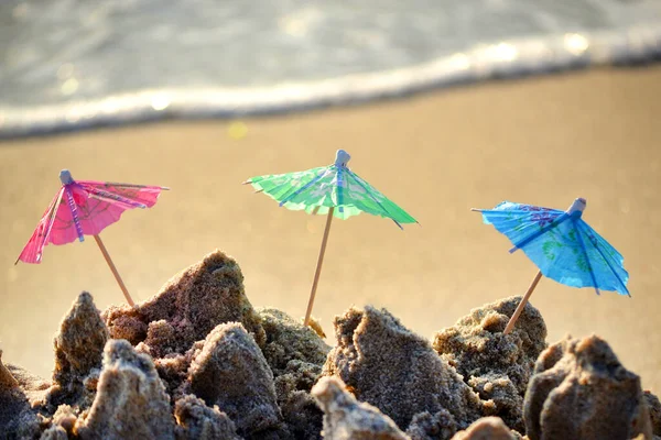 Três pequenos guarda-sóis de praia feitos de papel para coquetel na areia — Fotografia de Stock