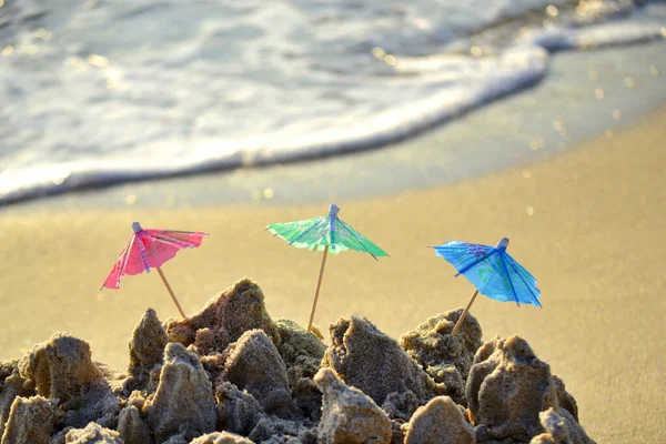 Três pequenos guarda-sóis de praia feitos de papel para coquetel na areia — Fotografia de Stock