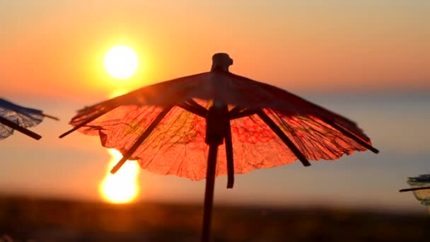 Paper cocktail umbrellas in sand on seashore at sunset dawn close-up. — Stock Video