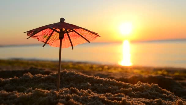 Ombrelli da cocktail di carta in sabbia in riva al mare all'alba del tramonto primo piano. — Video Stock