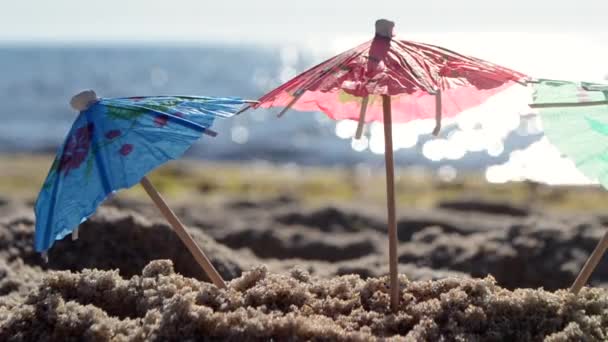 Ombrelli da cocktail di carta in sabbia in riva al mare nella soleggiata giornata estiva primo piano — Video Stock