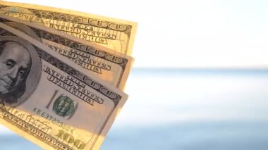 Deniz yüzeyinin arka planında 300 dolarlık banknotlar. 100 dolar nakit.