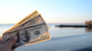 Deniz yüzeyinin arka planında 300 dolarlık banknotlar. 100 dolar nakit.