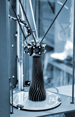 3D yazıcıda yapılmış siyah bir vazo çalışma yüzeyinde duruyor.