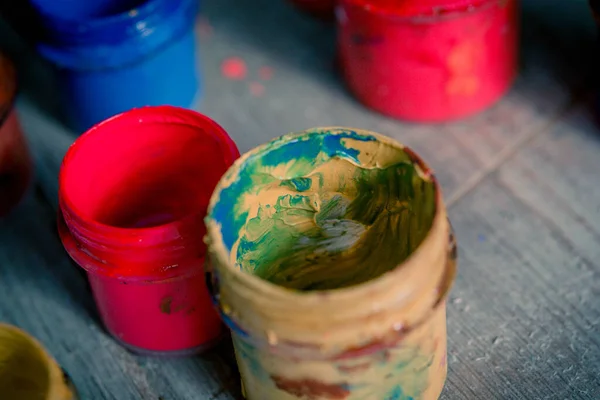 Muitos pequenos jarros de pintura com cores diferentes em uma superfície de madeira — Fotografia de Stock