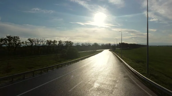 Drone rises above wet asphalt road for cars between sown fields — Stock Photo, Image